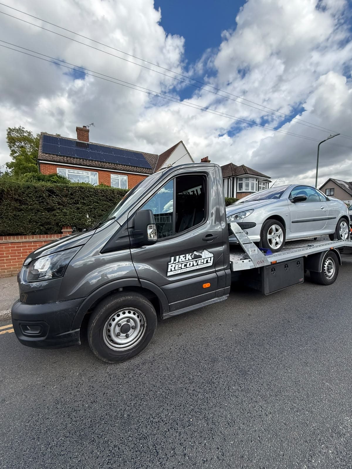 J&K Recovery truck with a silver convertible loaded on the flatbed outside a house