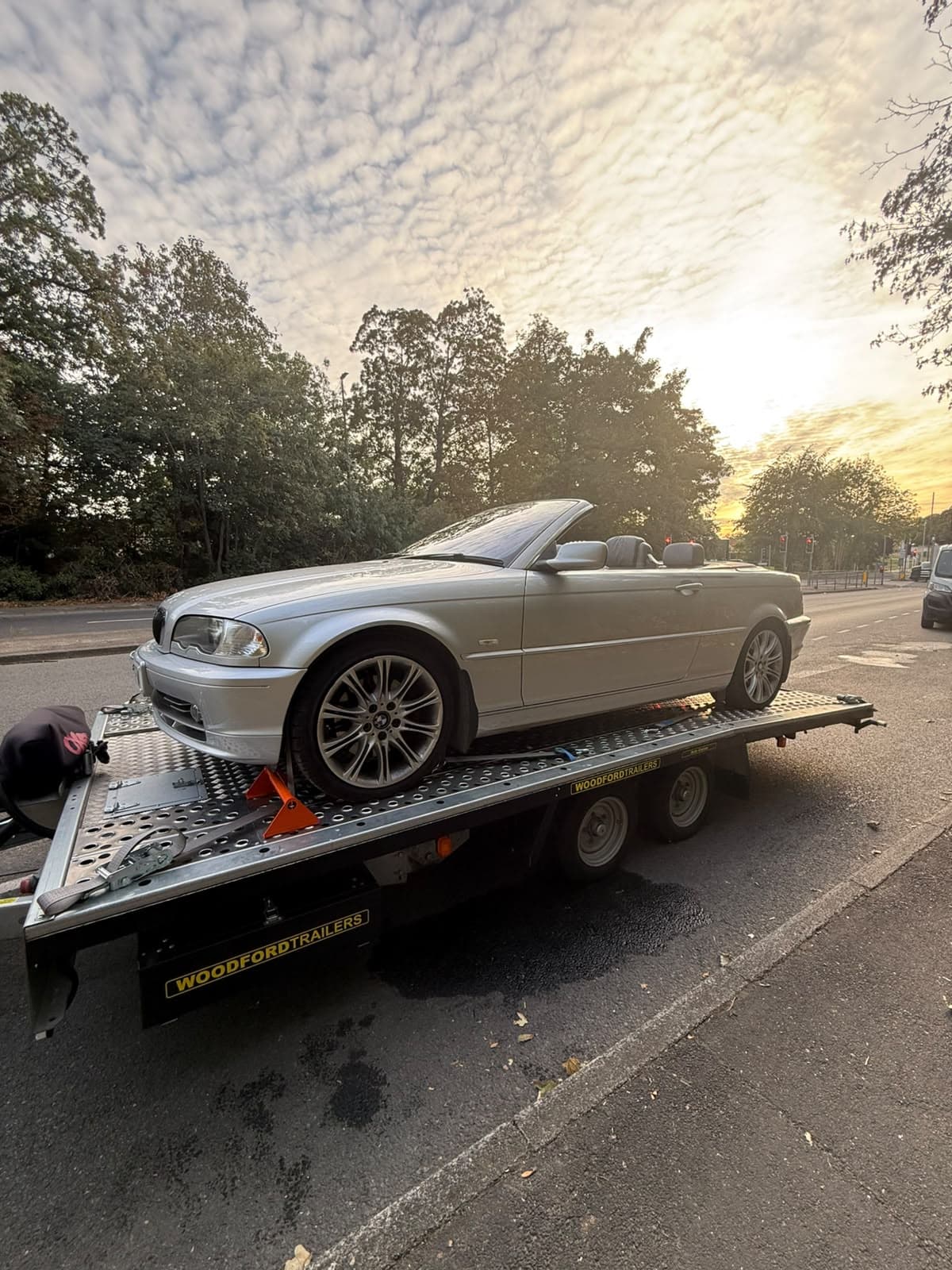 Silver BMW convertible secured on a car transporter trailer at sunset