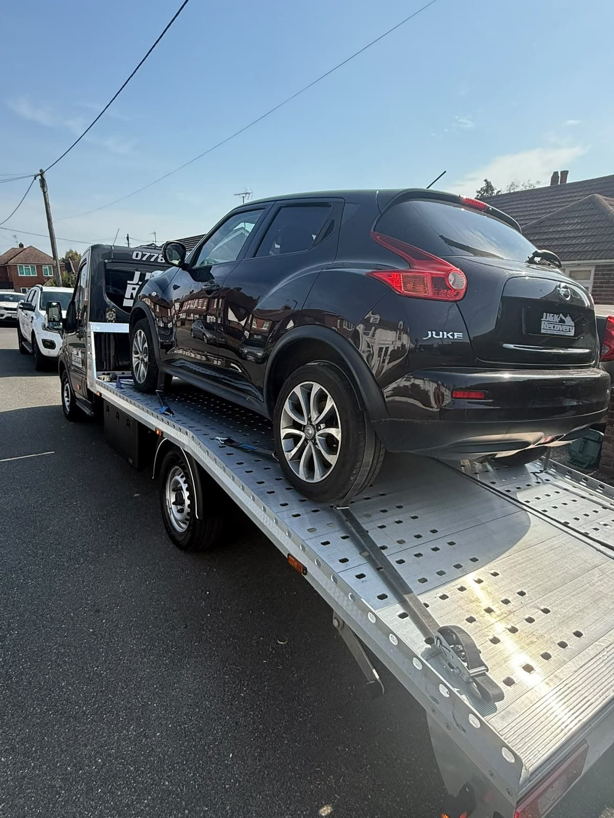 Black Nissan Juke loaded onto a J&K Recovery flatbed truck outside a home